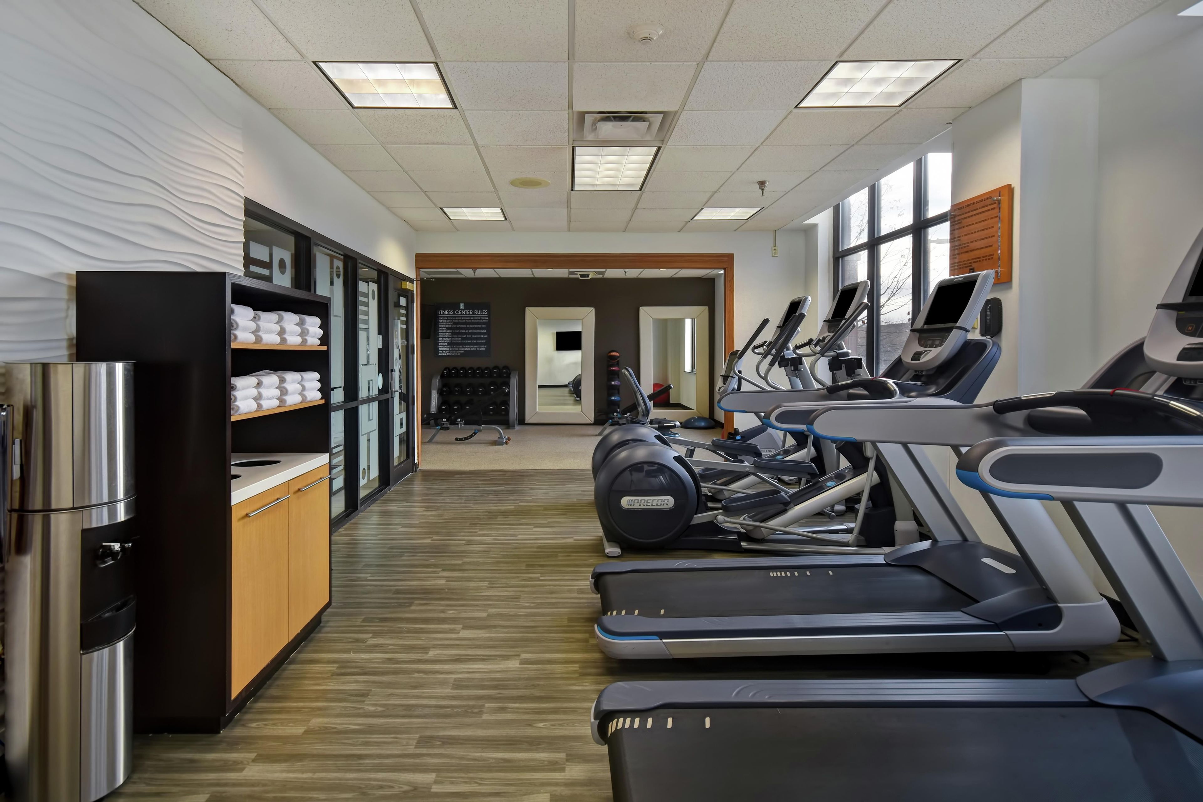 Une salle de sport équipée de tapis de course, de poids et d’un miroir.