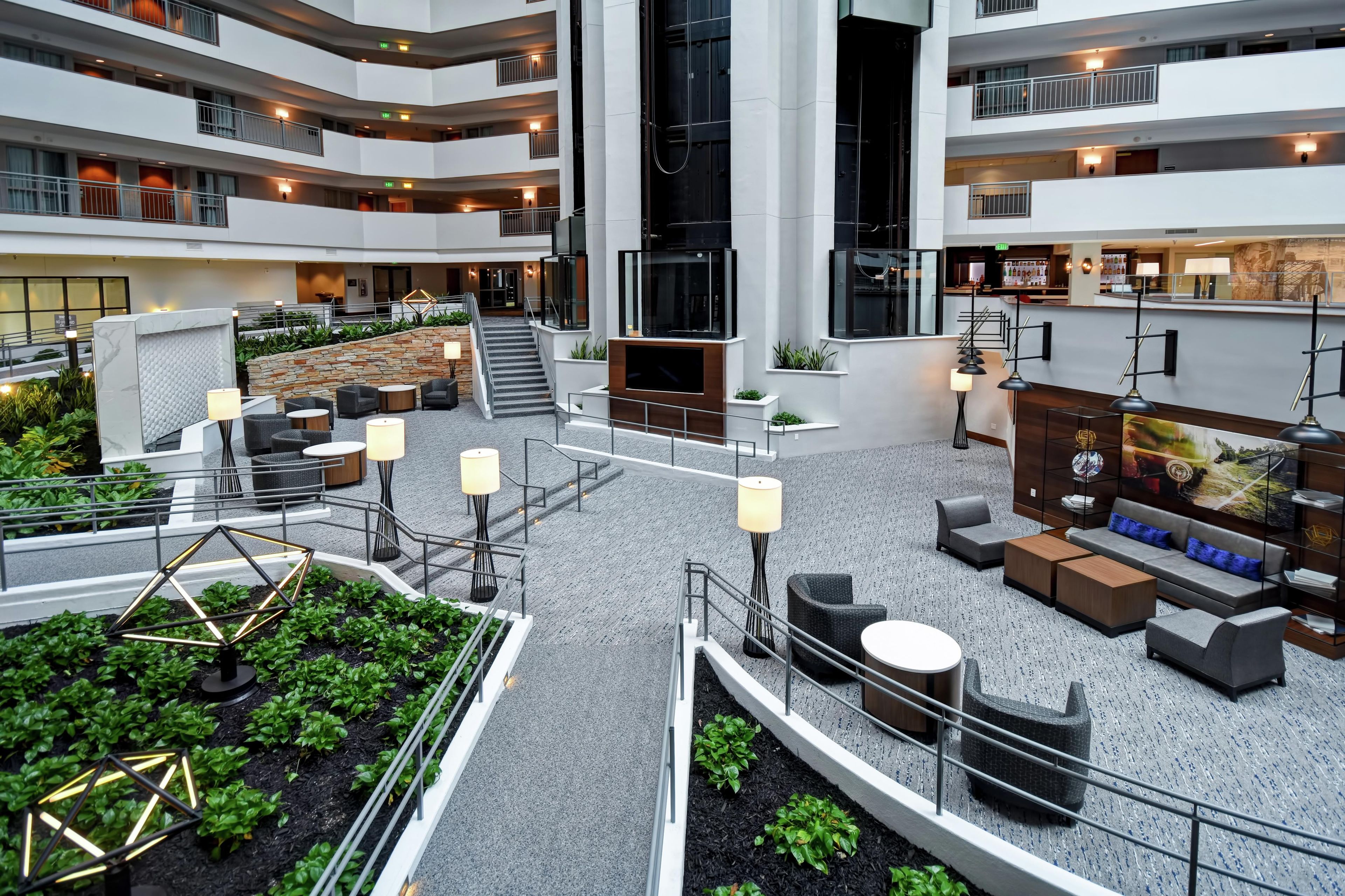 Vestíbulo de hotel de varios niveles con una escalera central, zonas de estar y un área de bar/lounge.