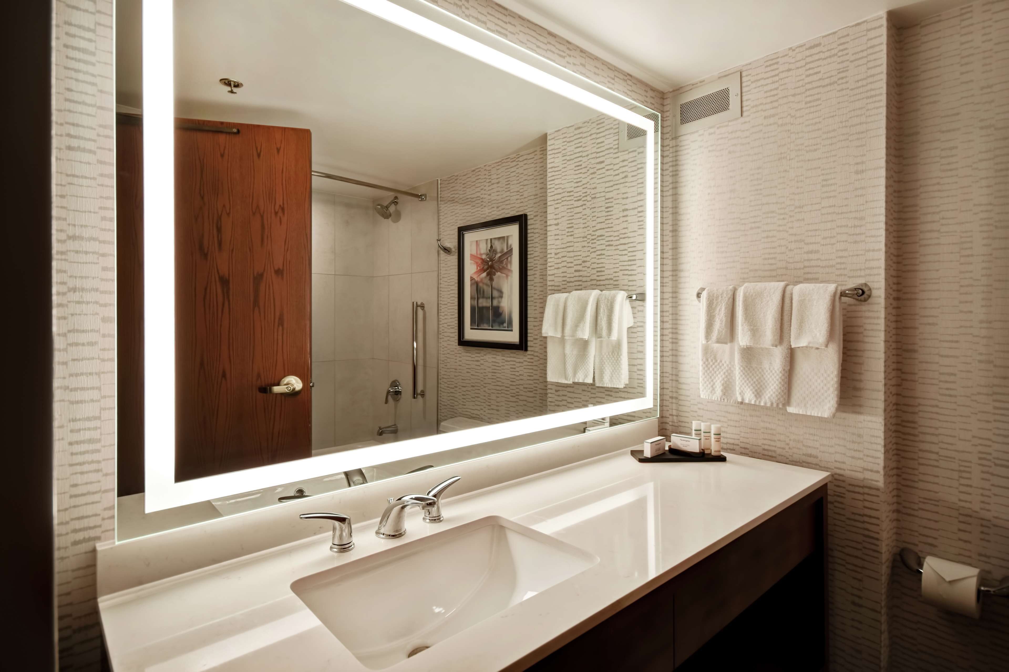 A modern bathroom with a large mirror, two sinks, and a shower.