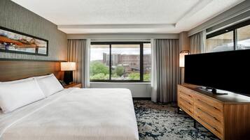 A hotel room with a large bed, a TV, a dresser, and a window with a city view.