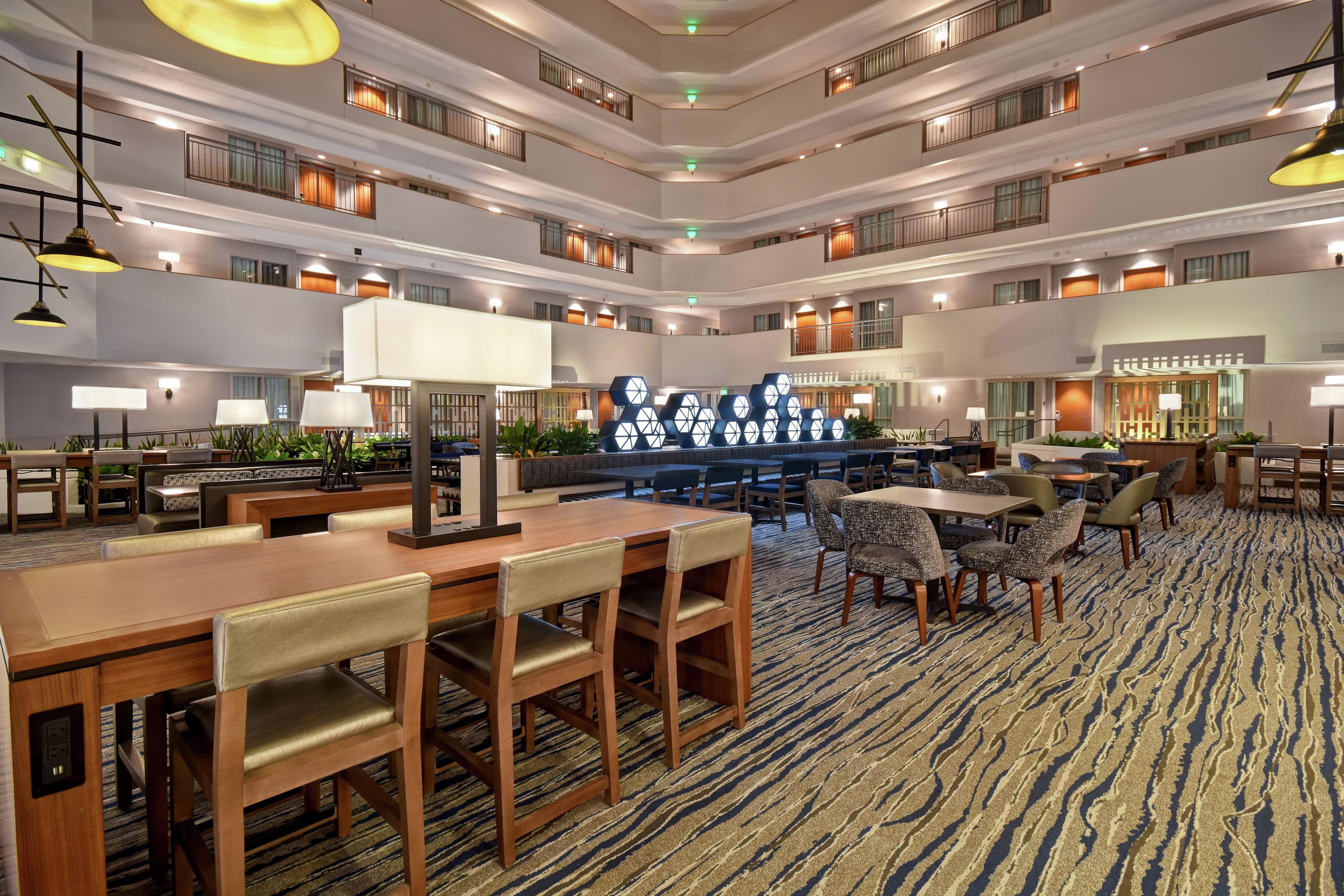 A multi-level hotel lobby with dining areas, seating arrangements, and a central decorative feature.