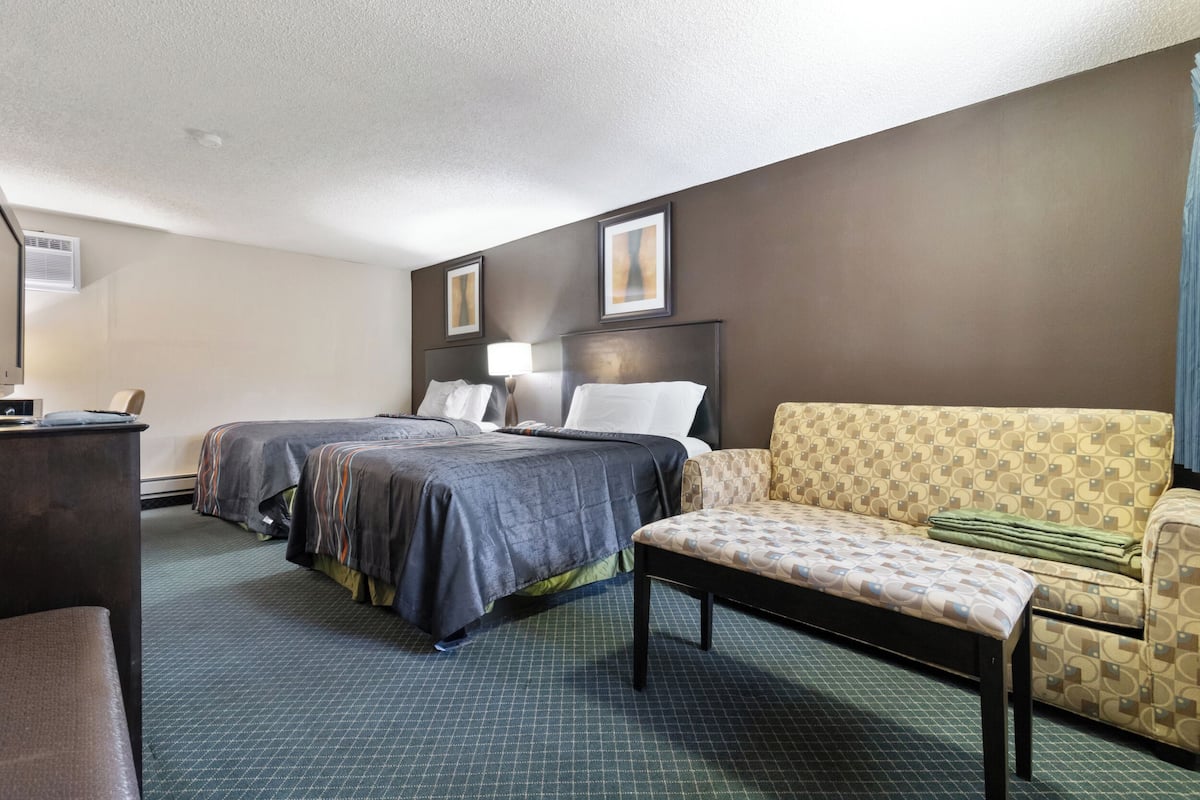 Une chambre d’hôtel avec deux lits, un canapé, un bureau et une lampe.