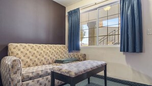 A room with a patterned sofa, a small table, and a window with curtains. - Economy Inn Barstow (Barstow)