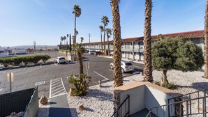 A parking lot with palm trees, a building with a red roof, and a clear blue sky. - Economy Inn Barstow (Barstow)