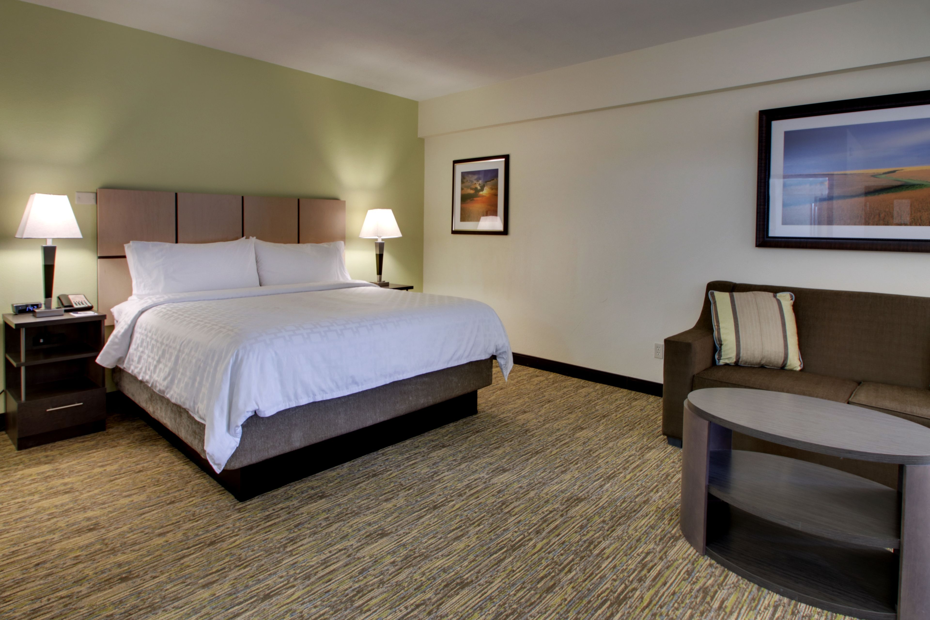 Quarto de hotel com uma cama, duas mesas de cabeceira com abajures, um sofá e uma pequena mesa.