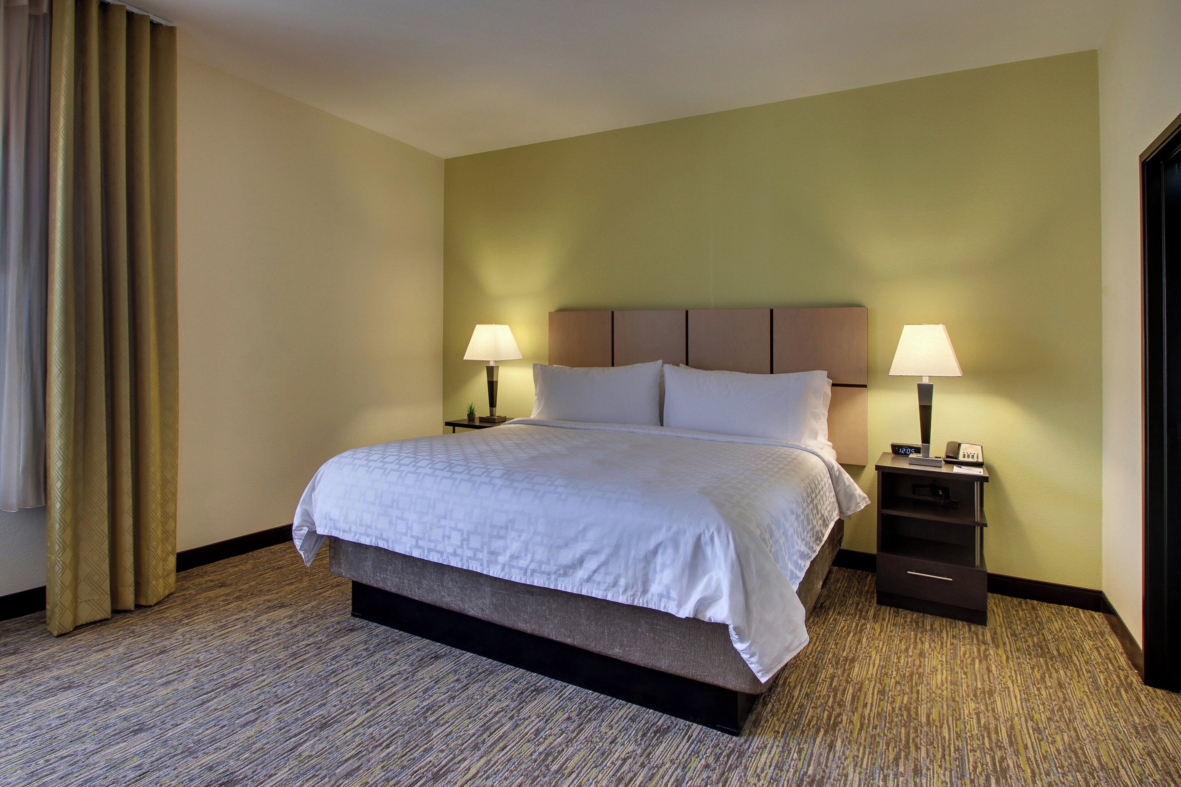 A hotel room with a bed, two bedside lamps, a nightstand, and a carpeted floor.