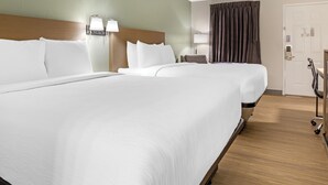 Une chambre d’hôtel avec deux lits, une tête de lit en bois, une table de chevet avec une lampe, une porte avec une serrure et une fenêtre avec des rideaux.