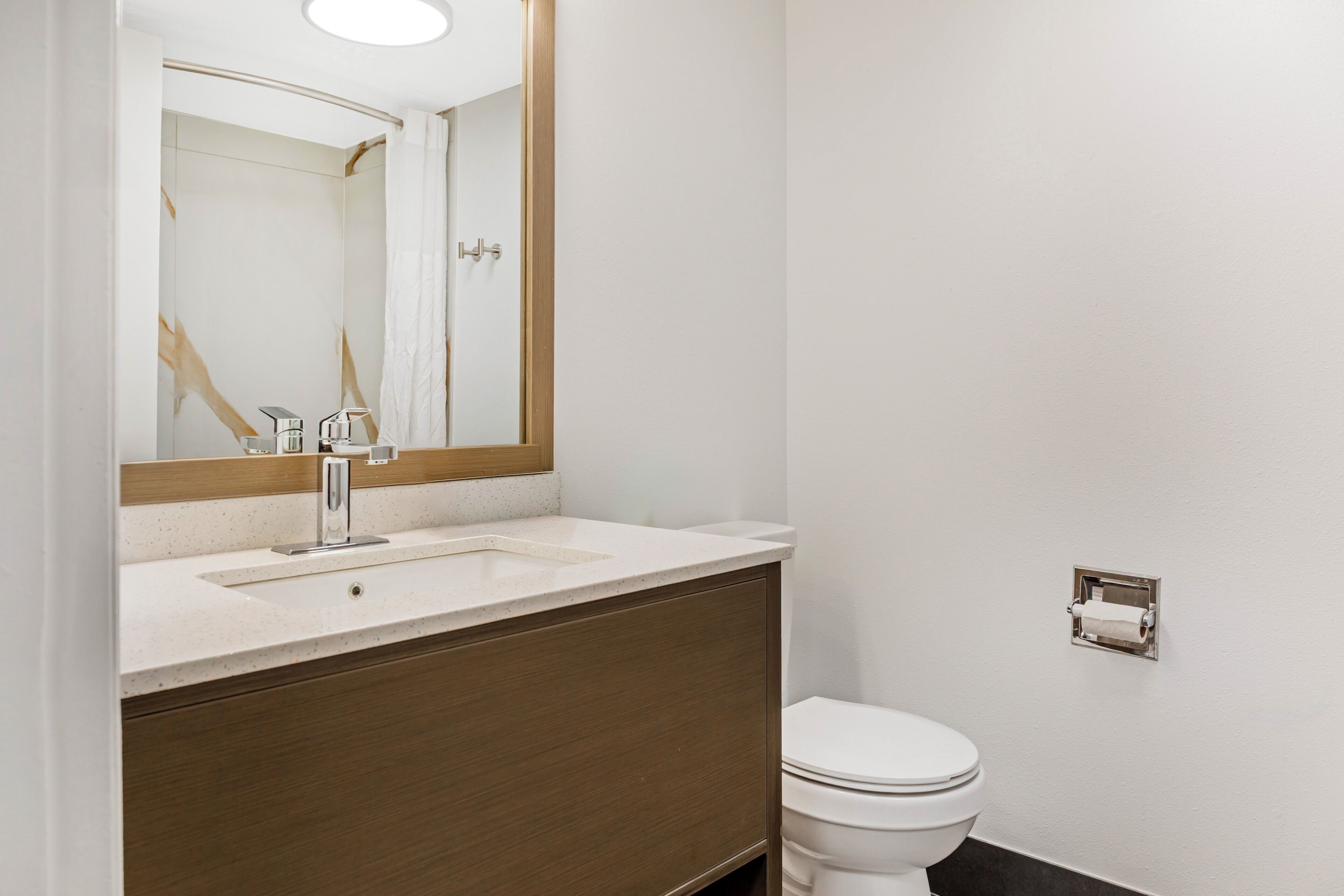 A bathroom with a white sink, a mirror, a toilet, and a towel dispenser.