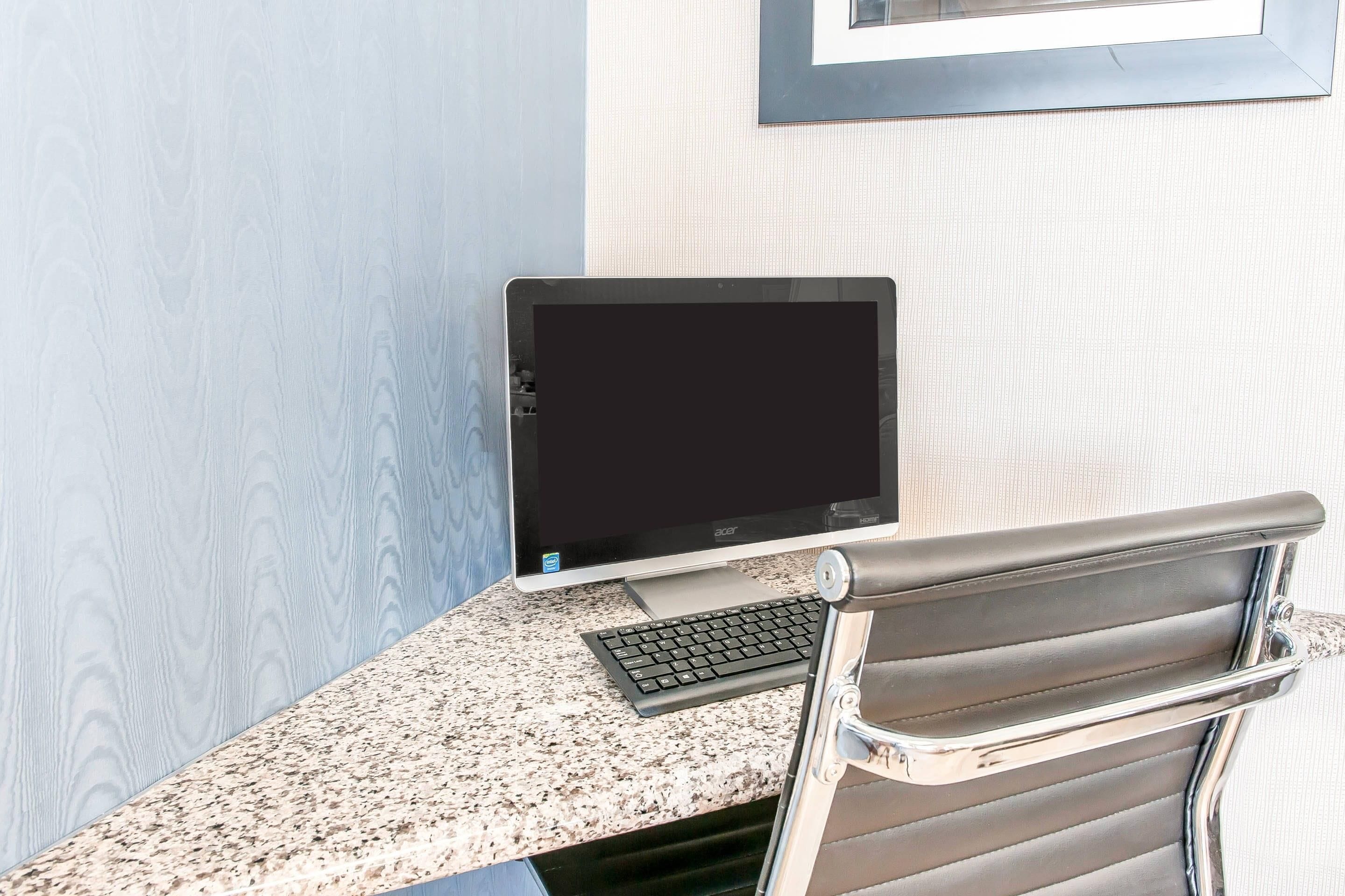 A computer desk with a monitor, keyboard, and a chair.