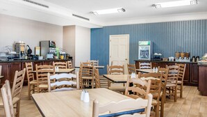 A hotel dining area with wooden tables and chairs, a coffee station, and a refrigerator.