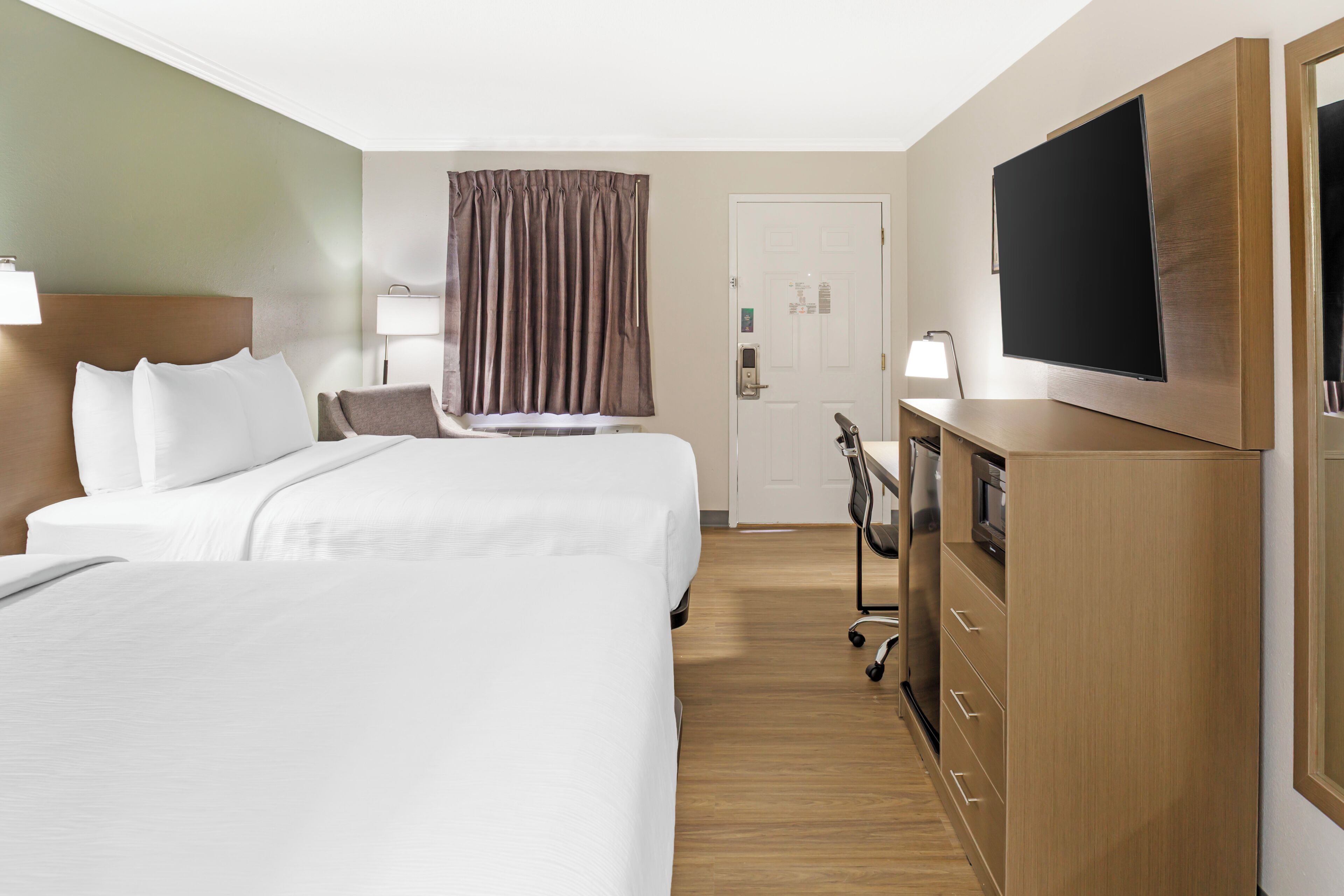 A hotel room with two beds, a television, a desk with a lamp, and a wardrobe.