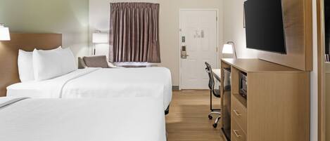 A hotel room with two beds, a television, a desk with a lamp, and a wardrobe.
