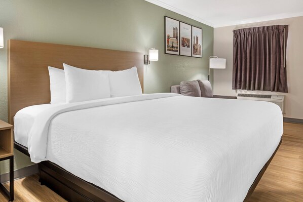 A large bed with white linens, a wooden headboard, a nightstand, a wall-mounted lamp, a framed cityscape picture, and a window with curtains. - Quality Inn Findlay (Findlay)