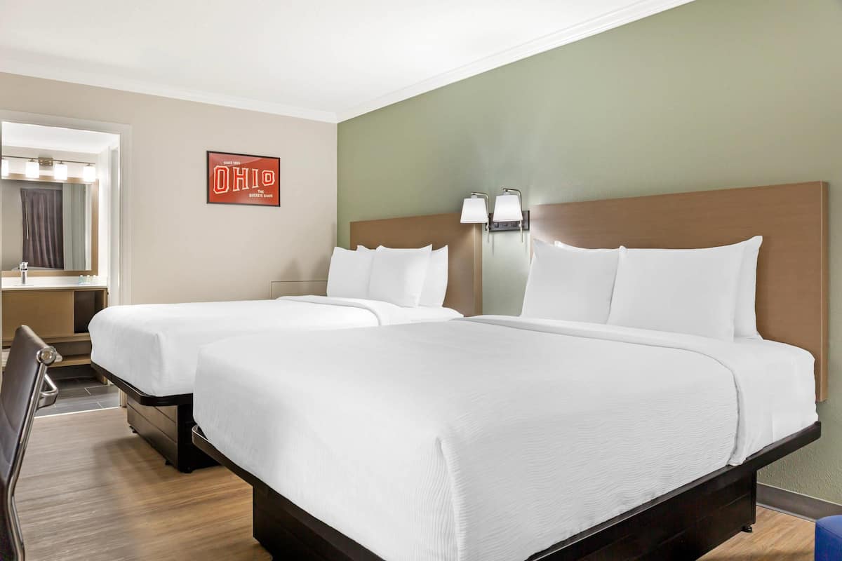 A hotel room with two beds, a mirror, a sign, and a nightstand.