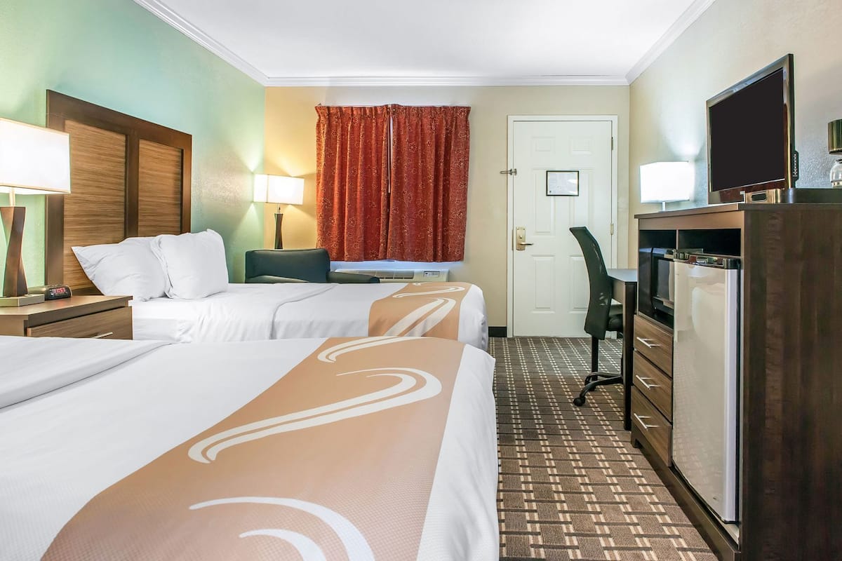 A hotel room with two beds, a desk, a chair, a television, and a refrigerator.