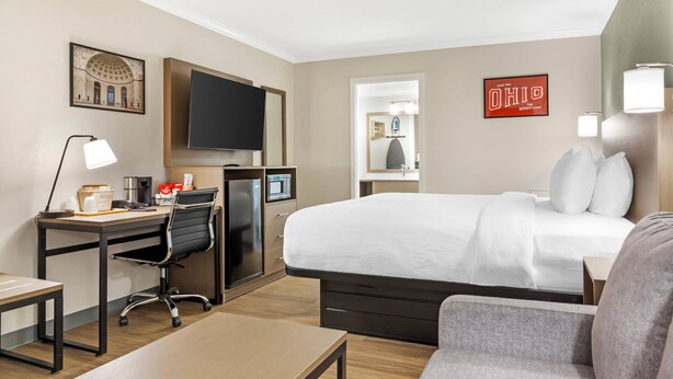 A hotel room with a bed, desk, chair, TV, and a mirror.