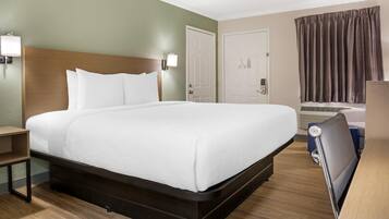 A hotel room with a large bed, a nightstand, a desk, a chair, and a window with curtains.