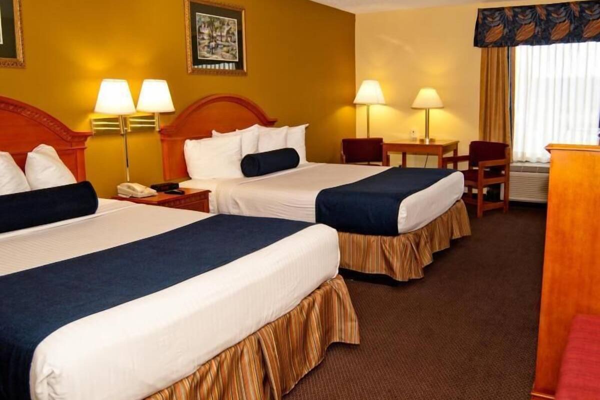 A hotel room with two beds, a desk, a chair, and a telephone.