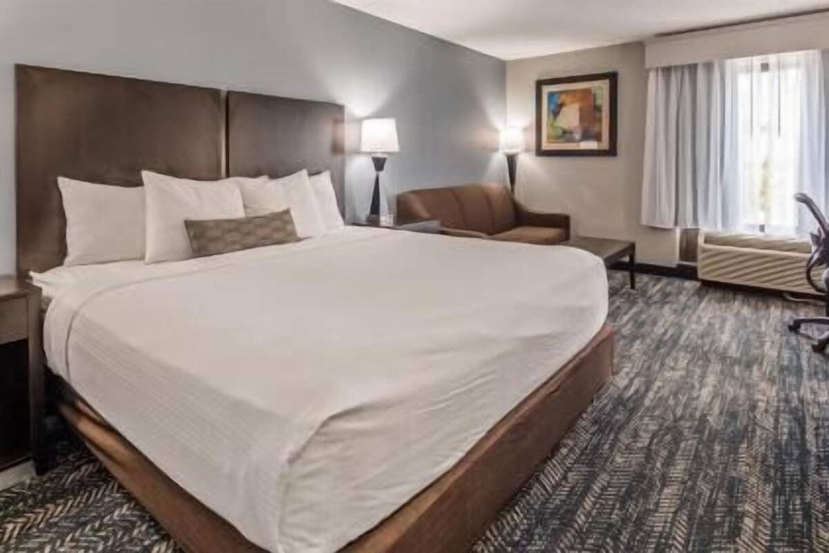 A hotel room with a large bed, a desk, a chair, a lamp, and a painting on the wall.