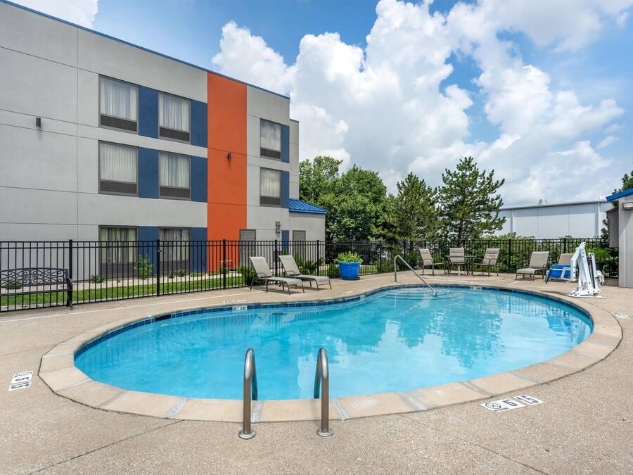 Una piscina con una escalera metálica, rodeada por una valla y contigua a un edificio de varios pisos con fachada azul y naranja.