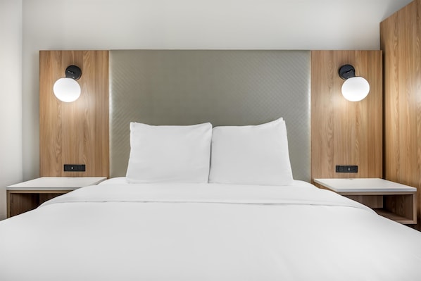 A modern hotel room with a large bed, two bedside tables, and wall-mounted lighting.