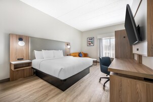 Habitación de hotel con cama, mesitas de noche, escritorio, silla, televisor y ventana con cortinas.