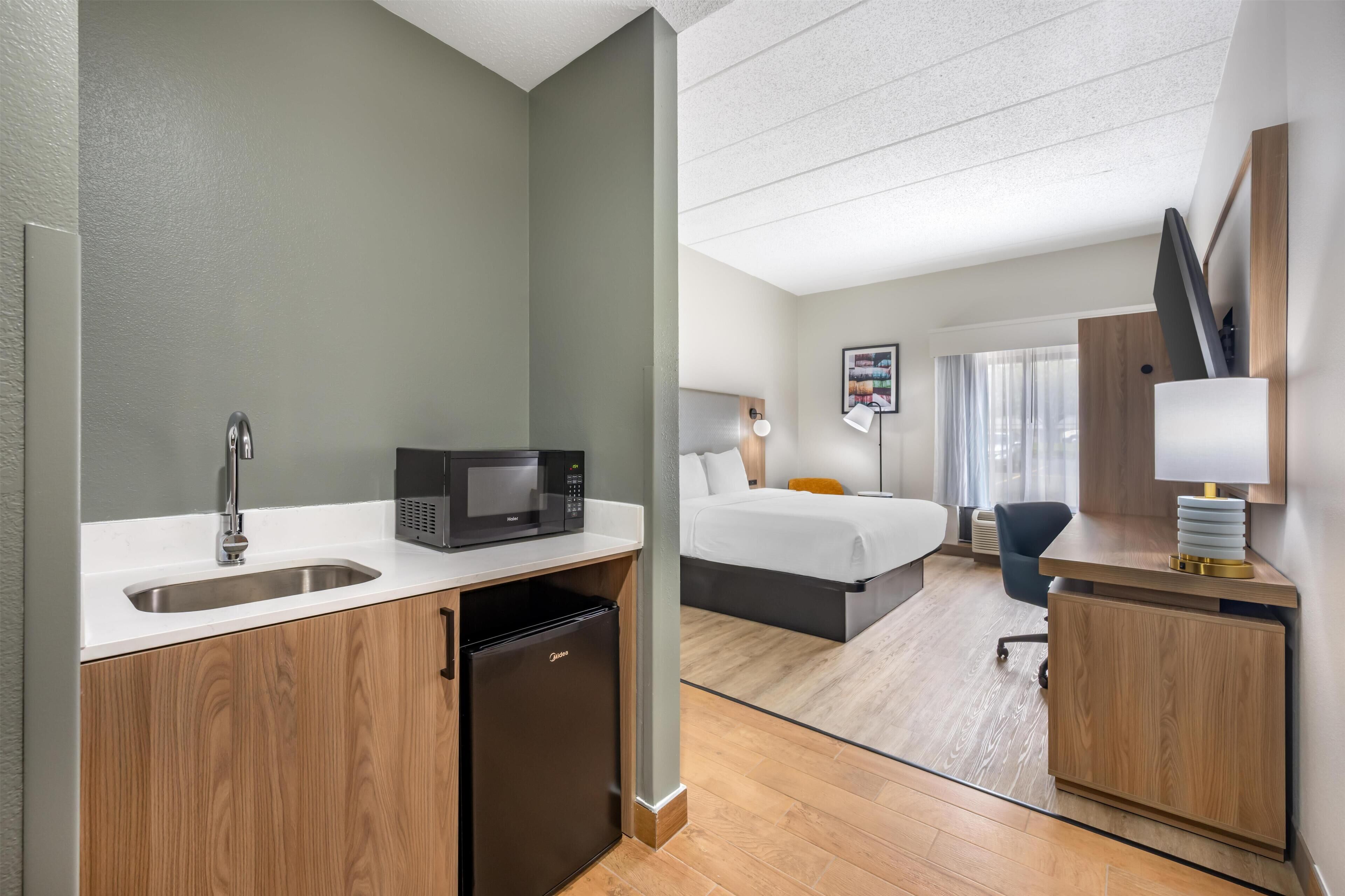 Una habitación de hotel con kitchenette, cama, escritorio y silla.