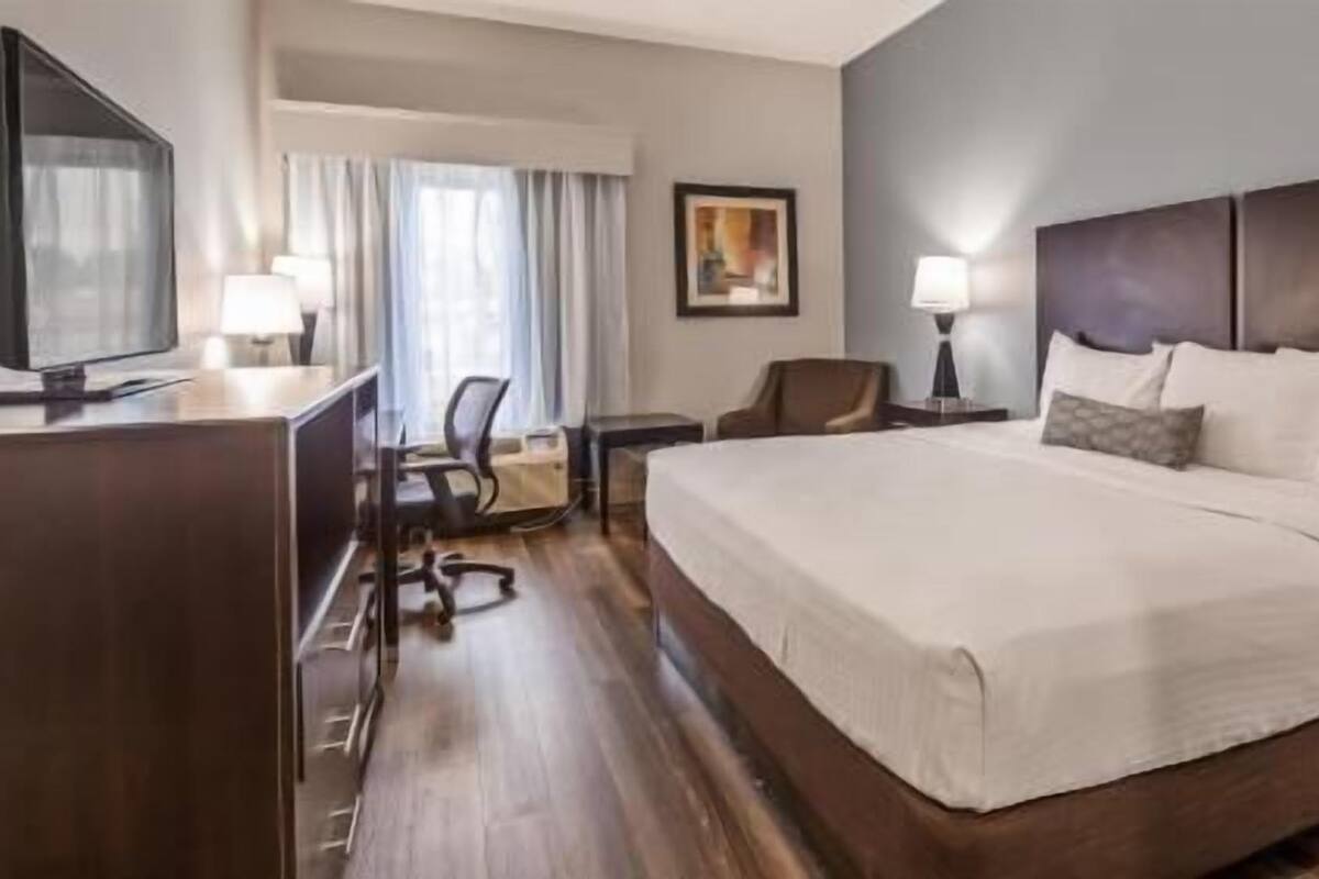 A hotel room with a large bed, a desk with a computer, a chair, and a TV.