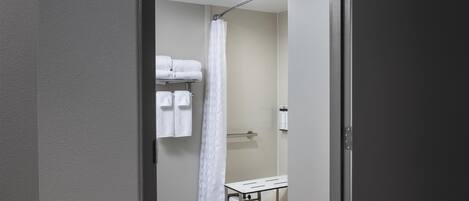 A modern bathroom with a shower, a towel rack, and a bench.
