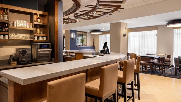 Un espace bar moderne, doté d’un long comptoir, de tabourets de bar et de différentes bouteilles et verres exposés sur des étagères.