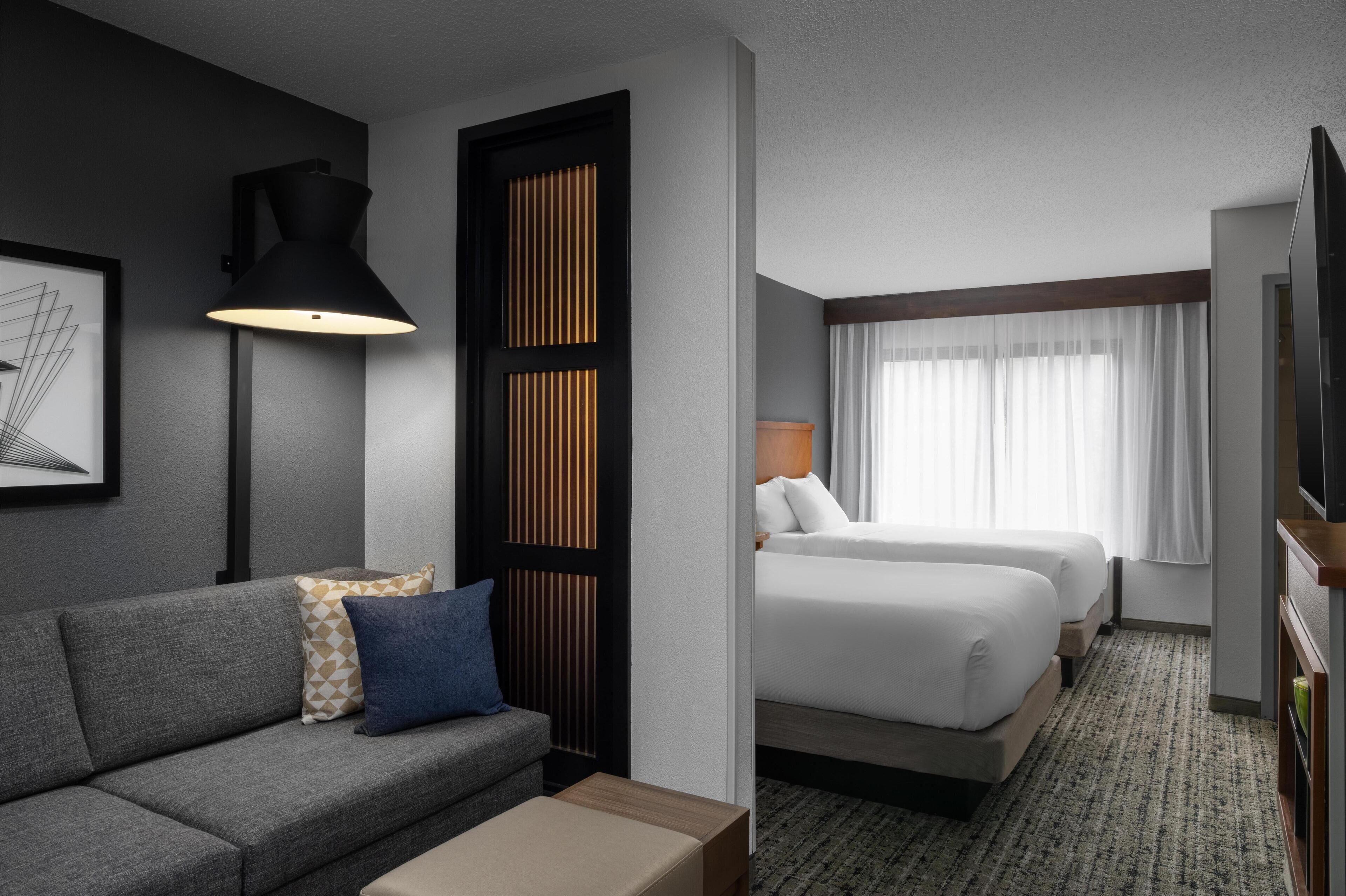 A hotel room with a sofa, two beds, a TV, and a large window with curtains.