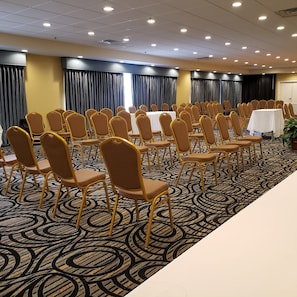 Un salón de conferencias con filas de sillas, mesas y una alfombra estampada.