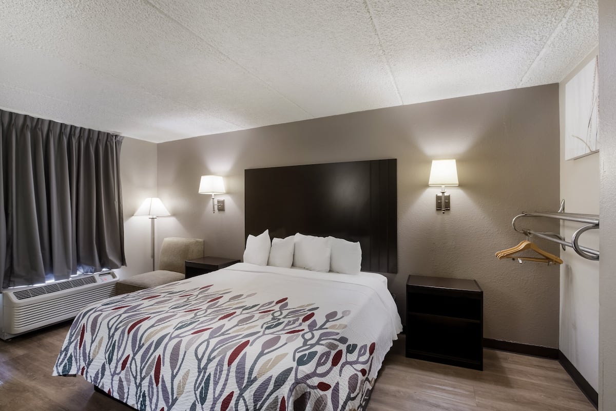 A hotel room with a bed, bedside lamps, a heater, a coat rack, and a wall-mounted TV.