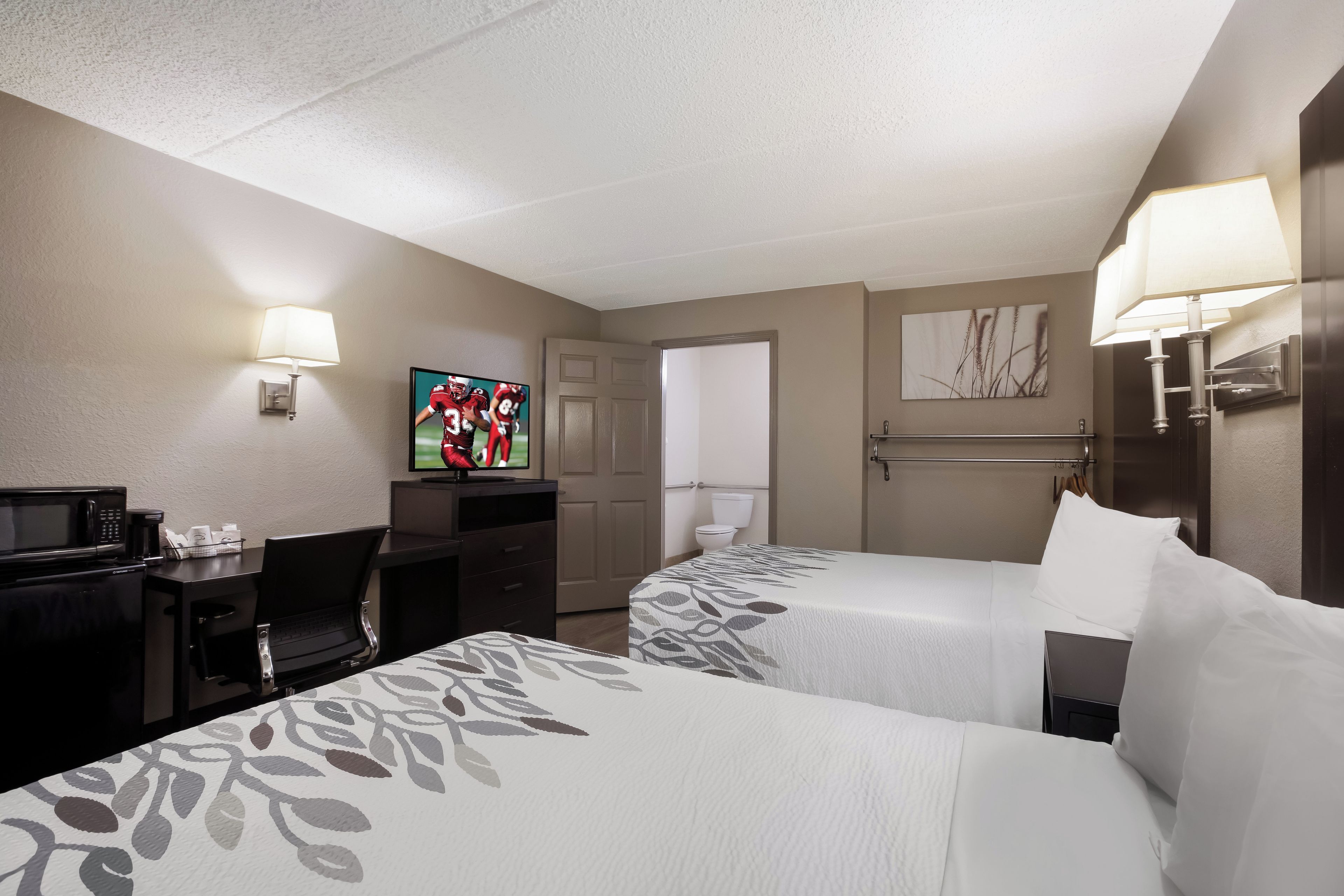 A hotel room with two beds, a desk with a laptop, a television, and a painting on the wall.