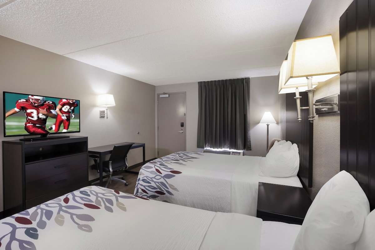 A hotel room with two beds, a desk, a television, and a lamp.