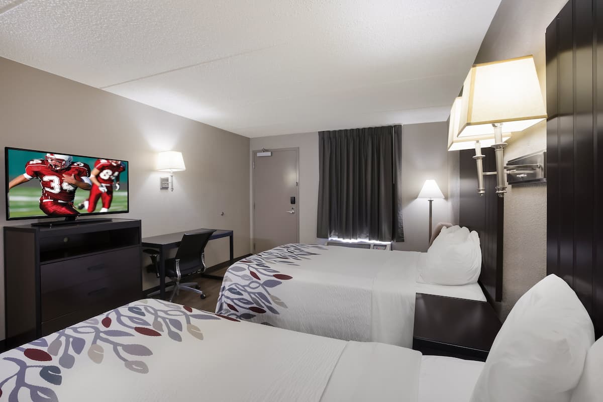 A hotel room with two beds, a desk, a television, and a lamp.
