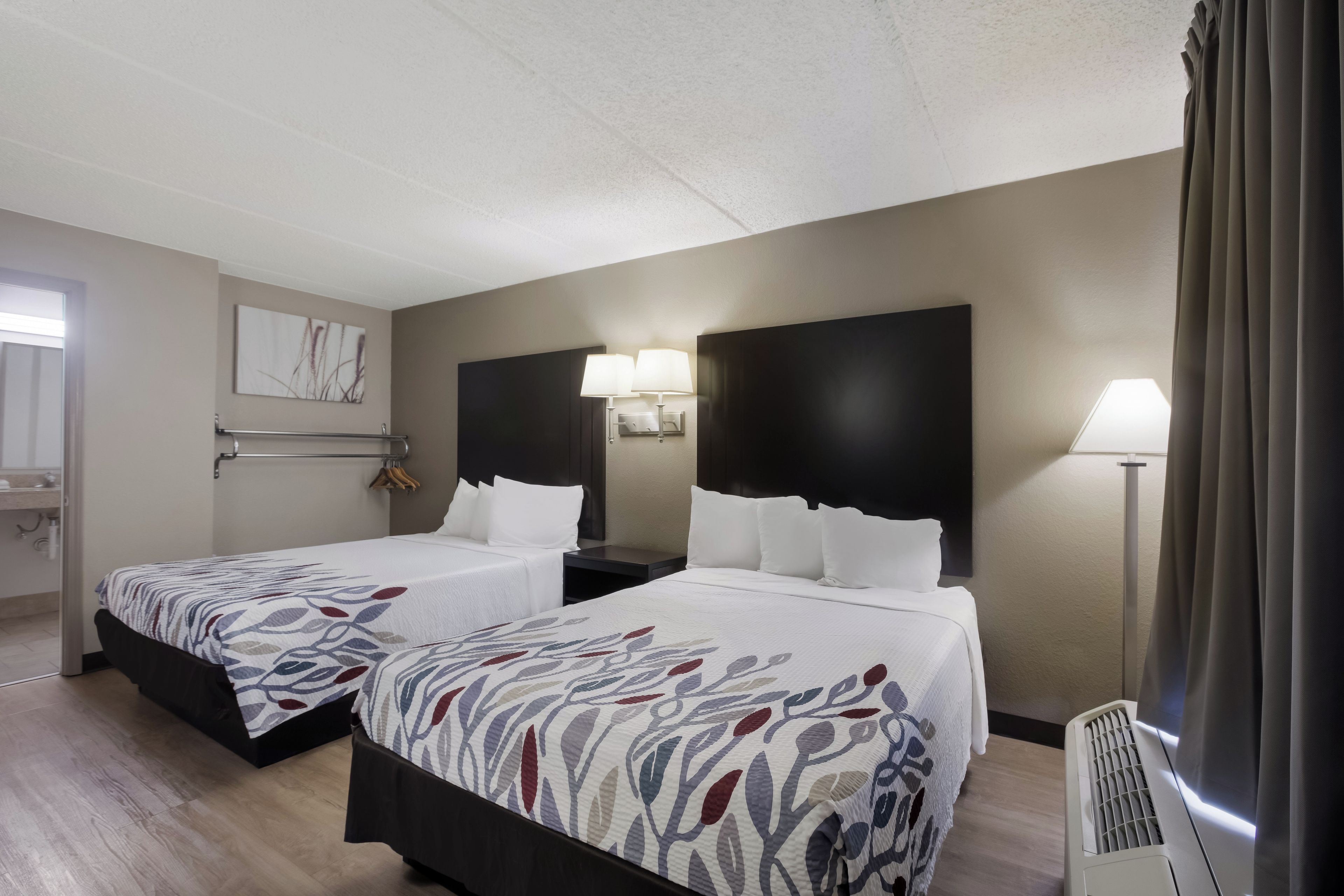 A hotel room with two beds, a bathroom, and a view of the outdoors.