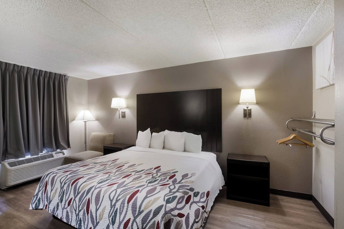 A hotel room with a bed, bedside lamps, a heater, a coat rack, and a wall-mounted TV.