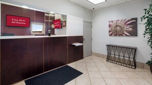 A reception area with a reception desk, a security camera, a free Wi-Fi sign, a window with a view, and a potted plant. - Red Roof Inn Atlanta Airport NE - Conley (Conley)