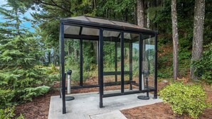 A glass-enclosed gazebo with a metal frame, surrounded by trees and a concrete base. - Red Roof Inn Atlanta Airport NE - Conley (Conley)