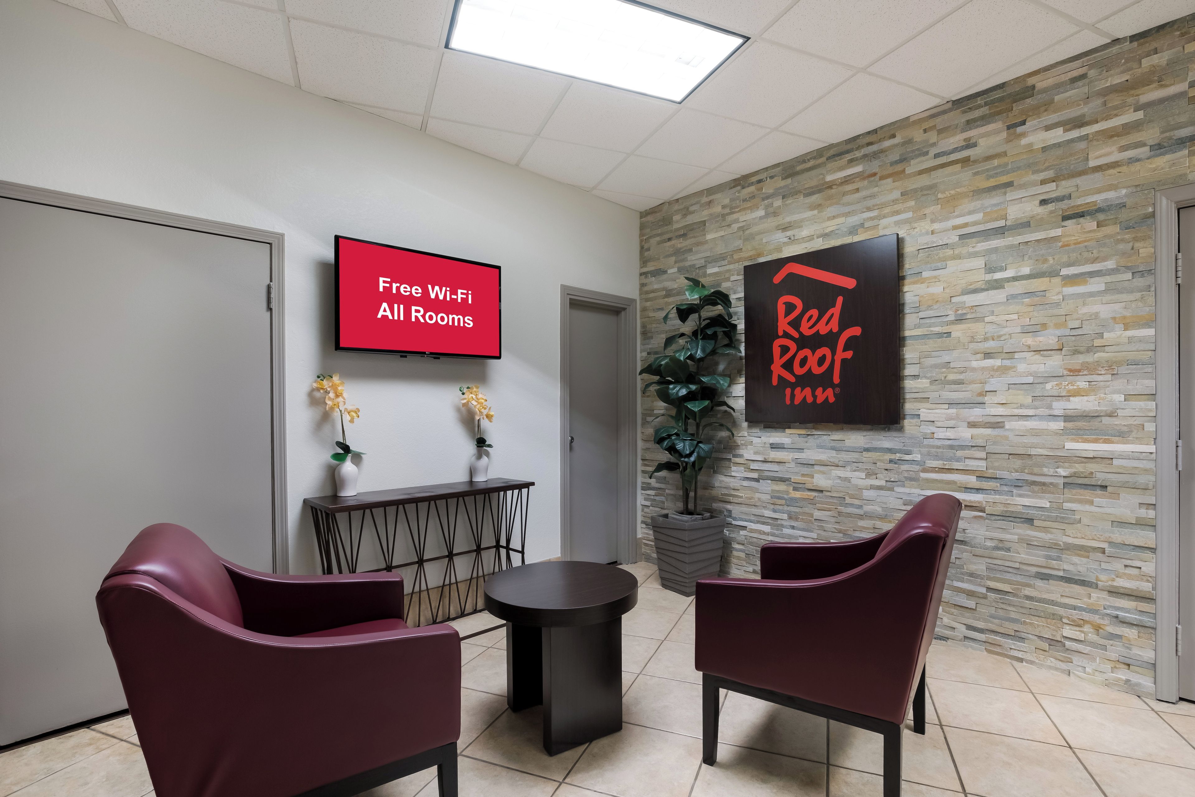 A reception area with a flat-screen TV displaying 'Free Wi-Fi All Rooms,' a Red Roof sign, and two potted plants.