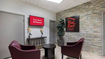 A reception area with a flat-screen TV displaying 'Free Wi-Fi All Rooms,' a Red Roof sign, and two potted plants.