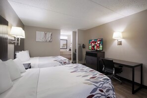 Habitación de hotel con dos camas, un escritorio, un televisor y una lámpara.