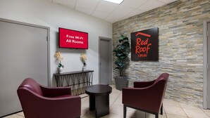 Un espace d’accueil doté d’un téléviseur à écran plat affichant le message « Wi-Fi gratuit dans toutes les chambres », d’une enseigne Red Roof Inn et d’un comptoir de réception agrémenté d’un vase de fleurs.