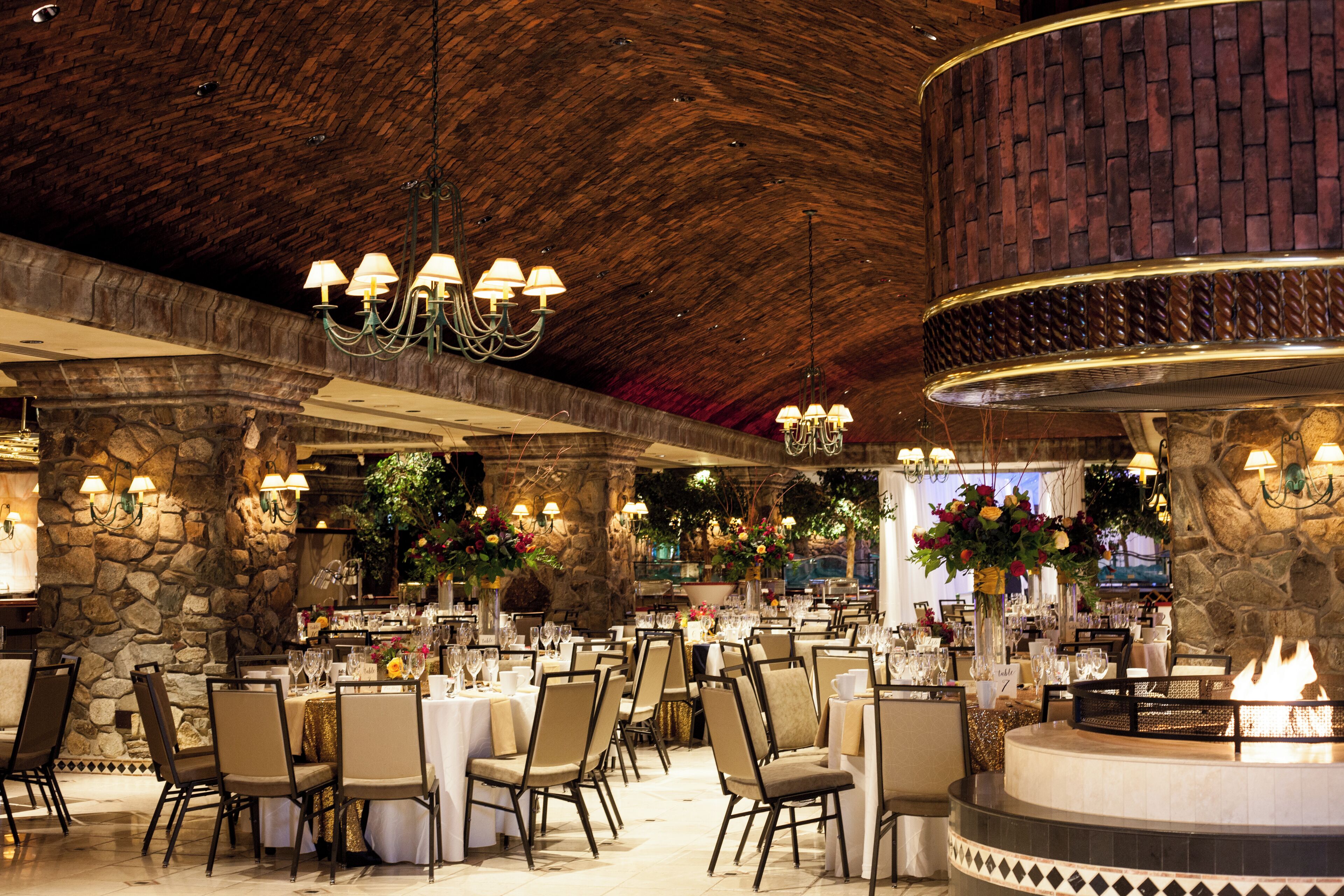 A restaurant with stone walls, chandeliers, and a central fire feature.