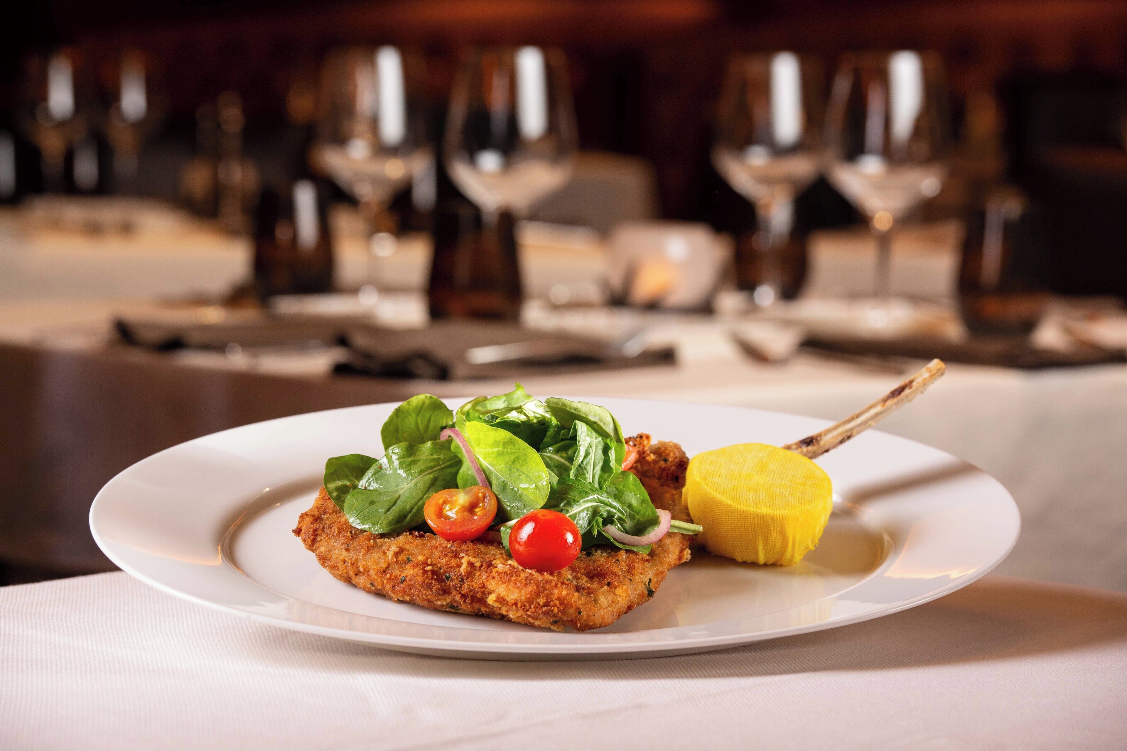 A plated dish with a breaded item, cherry tomatoes, spinach, and a lemon wedge.