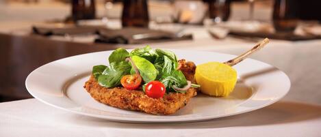 A plated dish with a breaded item, cherry tomatoes, spinach, and a lemon wedge.