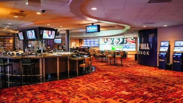 A hotel lobby with a bar area, multiple screens displaying sports content, and a large 'William Hill Sportsbook' sign.