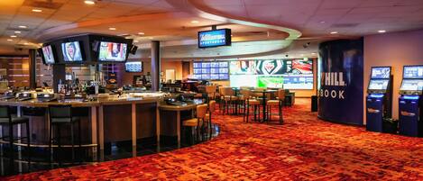 A hotel lobby with a bar area, multiple screens displaying sports content, and a large 'William Hill Sportsbook' sign.