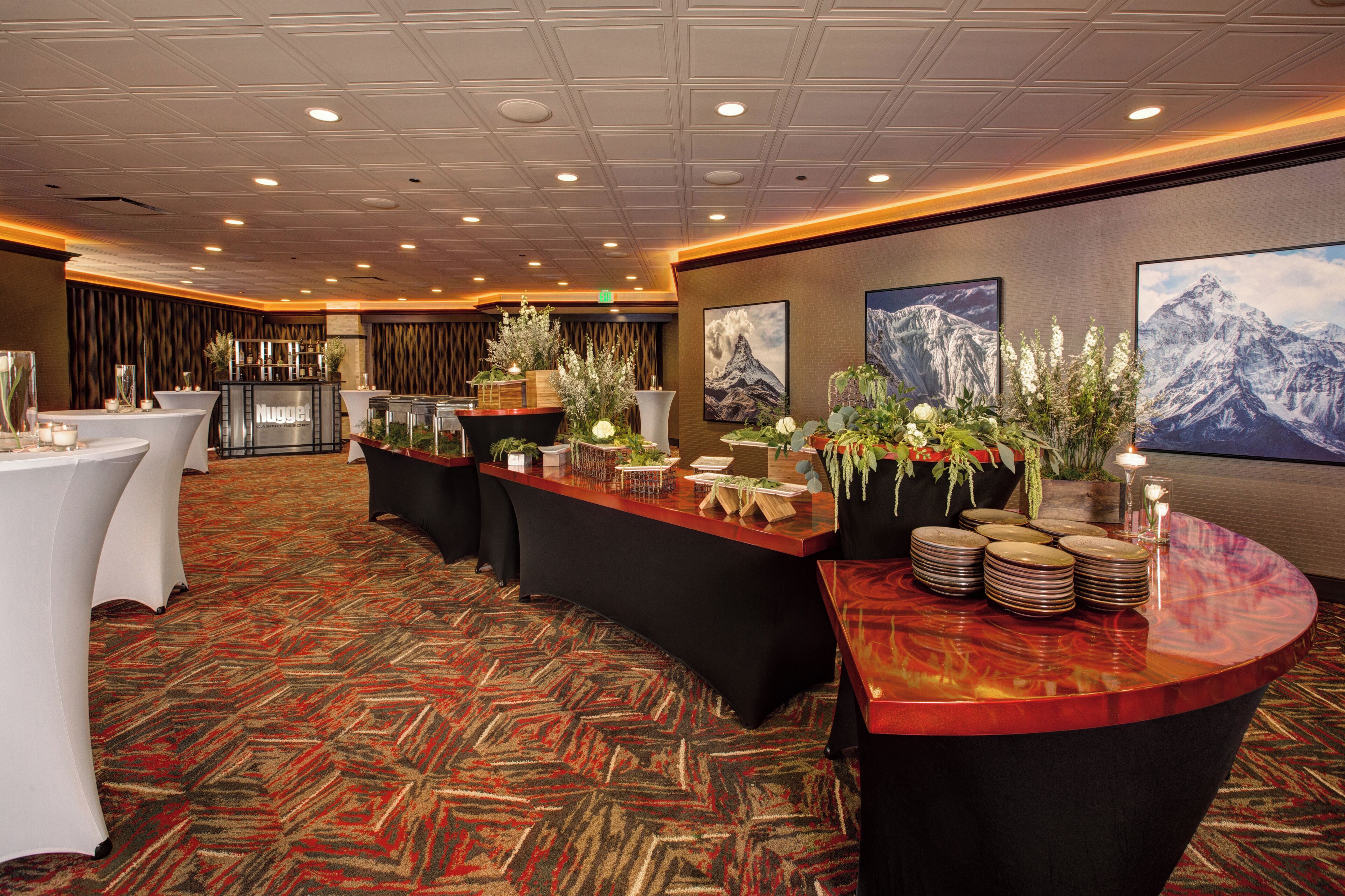 A hotel lobby with a reception desk, multiple tables, and decorative plants.
